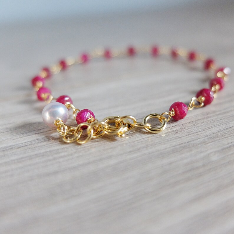 Op de afbeelding: Een gouden kettingarmband met roze edelsteen kralen en een enkele witte parel.