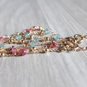 Peut inclure: Un collier en chaîne dorée avec des perles de pierres précieuses roses et bleues. Le collier a une chaîne délicate et est composé de plusieurs rangs.
