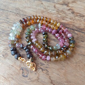 Op de afbeelding: Een veelkleurige edelsteenketting met een gouden sluiting. De ketting heeft gefacetteerde toermalijn kralen in roze, groen, bruin en geel. De kralen zijn geregen tot een uniek sieraad. De ketting is ongeveer 45 cm lang.