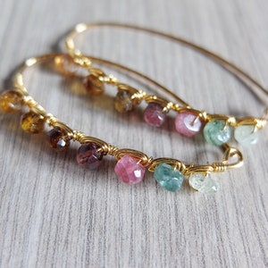 May include: Gold hoop earrings with a variety of gemstones including pink, green, and brown.
