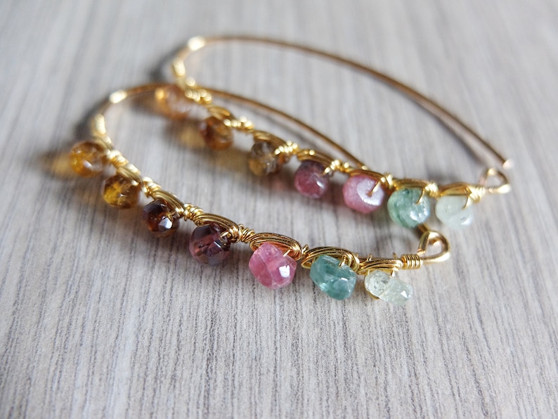 May include: Gold hoop earrings with a variety of gemstones including pink, green, and brown.