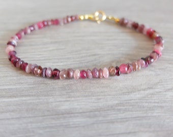 May include: A delicate pink and red gemstone bracelet with a gold clasp. The bracelet is made of small, round beads and is perfect for layering with other bracelets.
