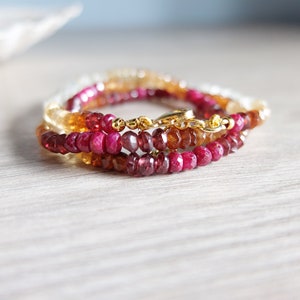Op de afbeelding: Een meerstrengige armband met rode, oranje en gele edelsteen kralen. De armband heeft een gouden sluiting.
