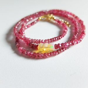 May include: A delicate pink gemstone necklace with a single opal bead in the center. The necklace is made of small, faceted beads and is layered for a more dramatic look.