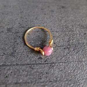 K&ouml;nnte beinhalten: Ein goldener Ring mit einem rosafarbenen Edelstein. Der Ring ist aus Draht gefertigt und der Edelstein ist in der Mitte des Rings eingesetzt.