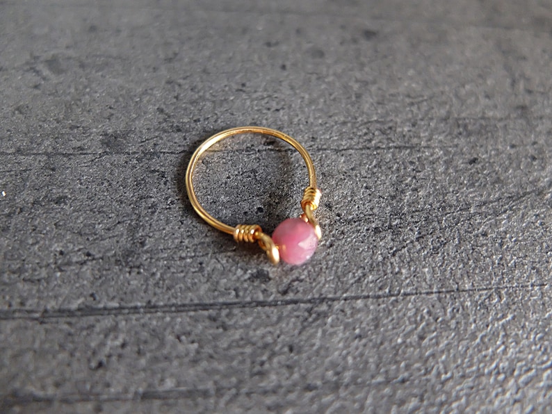 K&ouml;nnte beinhalten: Ein goldener Ring mit einem rosafarbenen Edelstein. Der Ring ist aus Draht gefertigt und der Edelstein ist in der Mitte des Rings eingesetzt.