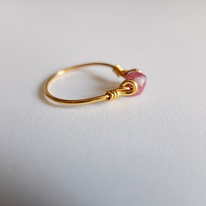 K&ouml;nnte beinhalten: Ein goldener Ring mit einem rosafarbenen Edelstein, der mit Draht umwickelt ist.