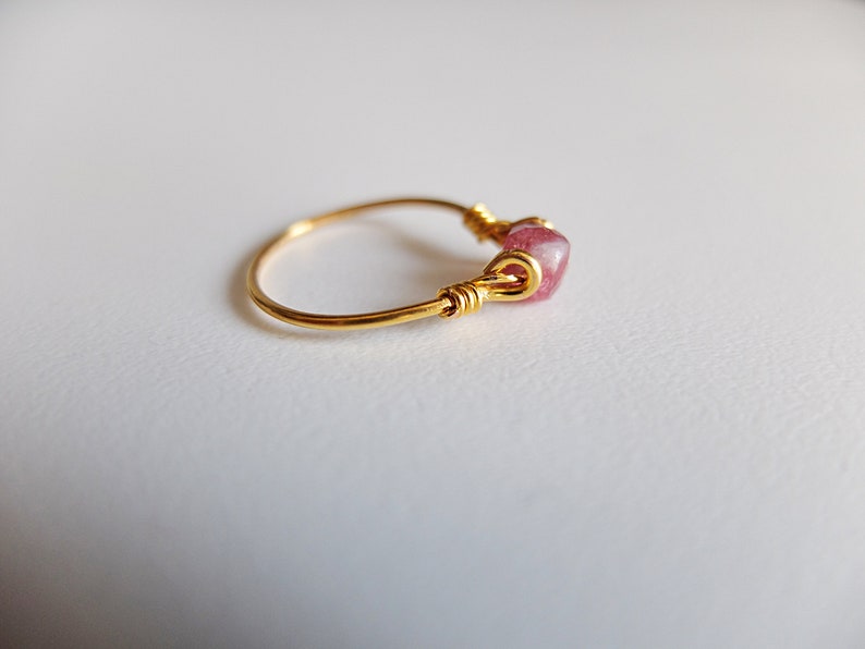 K&ouml;nnte beinhalten: Ein goldener Ring mit einem rosafarbenen Edelstein, der mit Draht umwickelt ist.