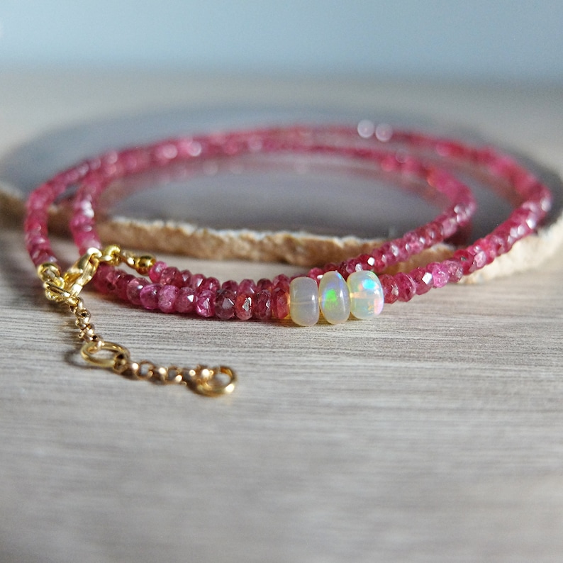 May include: A delicate gold chain necklace with pink gemstone beads and three opal beads.