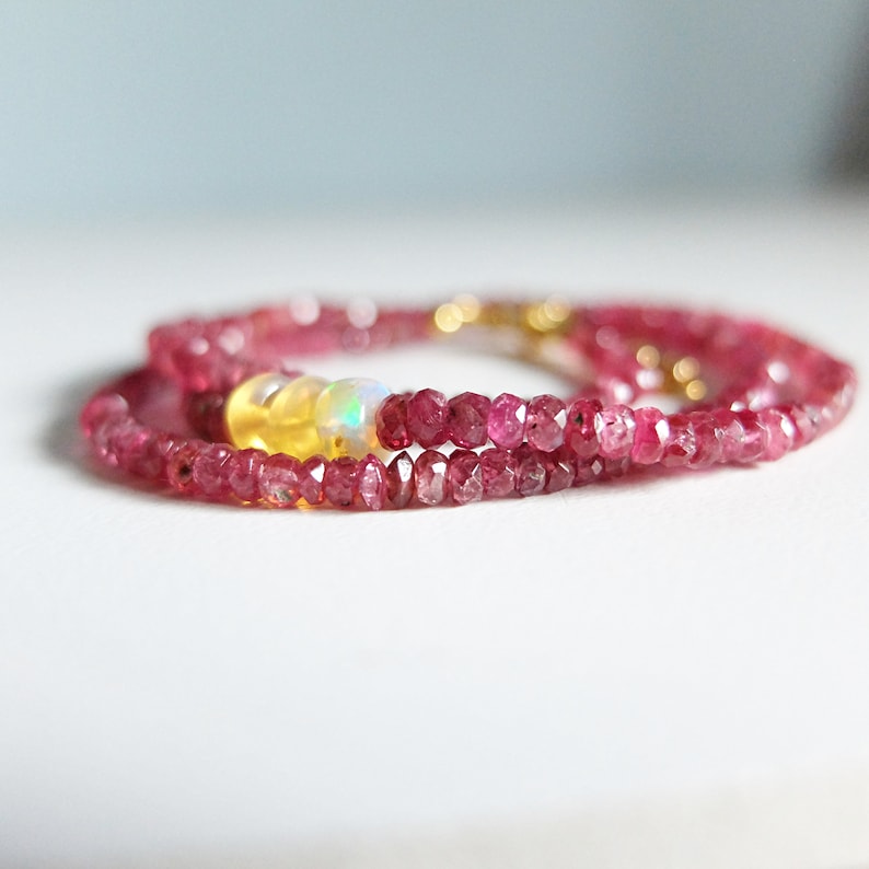 May include: A delicate gold chain necklace with pink and yellow gemstone beads. The necklace features a cluster of three beads, including a pink, yellow, and iridescent white bead.