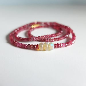 Op de afbeelding: Een delicate ketting gemaakt met kleine roze robijn kralen en drie iriserende opaalkralen.