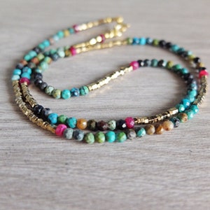 Puede incluir: Un collar de múltiples hilos con cuentas doradas y de piedras preciosas. El collar presenta cuentas turquesa, rosas, marrones y negras.