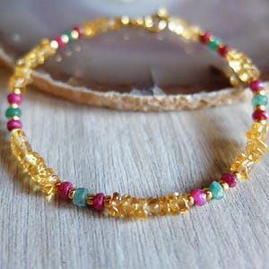 Könnte beinhalten: Ein zartes Armband mit einer Kombination aus goldenem Citrin, Rubin und Smaragd. Das Armband ist an einer Goldkette aufgereiht und schafft ein lebendiges und elegantes Accessoire. Die Edelsteine sind in einem Muster aus Gelb, Rot und Grün angeordnet.