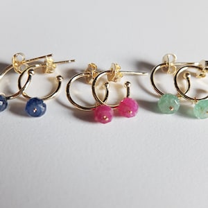 Könnte beinhalten: Drei Paar goldene Creolen mit Edelsteinbesatz. Die Ohrringe haben kleine, runde Edelsteine in Blau, Pink und Grün.