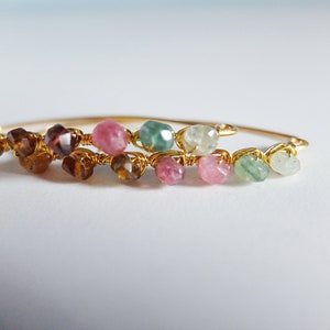 May include: A gold wire wrapped bracelet with a variety of colorful gemstones, including pink, green, and brown.