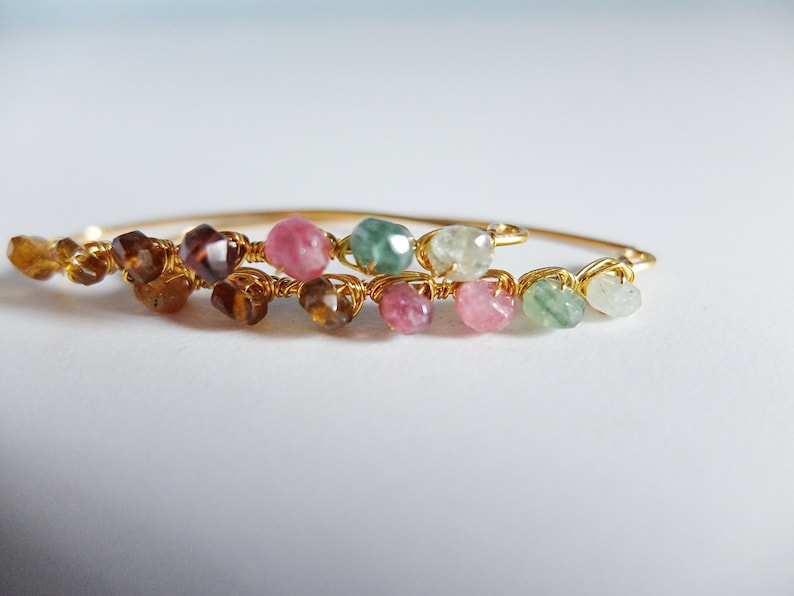 May include: A gold wire wrapped bracelet with a variety of colorful gemstones, including pink, green, and brown.