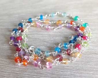 May include: A silver chain necklace with colorful gemstone beads. The beads are in a rainbow pattern and include pink, blue, green, yellow, orange, and red.