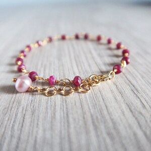 Op de afbeelding: Een delicate gouden kettingarmband met roze robijn kralen en een enkele roze parel bedel.