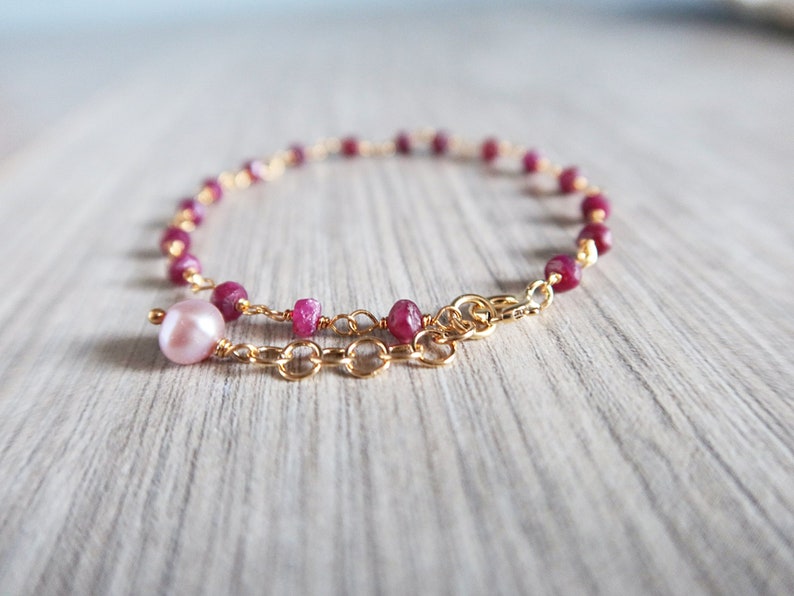 Op de afbeelding: Een delicate gouden kettingarmband met roze robijn kralen en een enkele roze parel bedel.