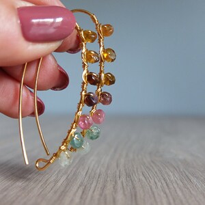 May include: Gold wire earrings with a cascade of colorful gemstones. The gemstones are in shades of green, pink, brown, and yellow.
