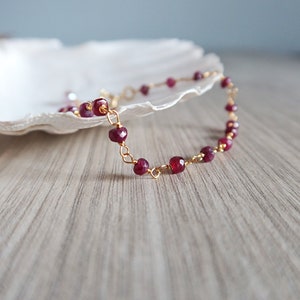 Op de afbeelding: Een delicate gouden kettingarmband met kleine, gefacetteerde robijnrode kralen.