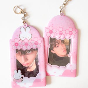 May include: Two pink keychains with photos inside. The keychains have a floral design with a bunny and flower accents. Each keychain has a silver-colored chain and clasp.