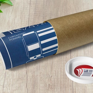 May include: A rolled up blue and white blueprint with the text "CHROMONIC POMMEL" is inside a brown cardboard tube. A white round sticker with a red logo of three stacked papers with a graph is on a wooden surface.