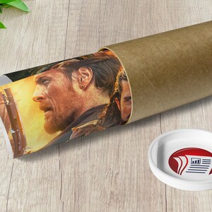 May include: A rolled-up poster featuring a close-up of a man's face with a beard and a gold earring. The poster is partially unrolled and shows a scene with a fiery background. The poster is in a brown cardboard tube.