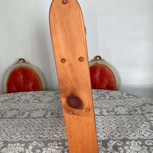 Puede incluir: Un soporte de madera con un acabado natural y una parte superior redondeada. El soporte tiene una serie de peque&ntilde;os clavos espaciados uniformemente a lo largo de los lados.