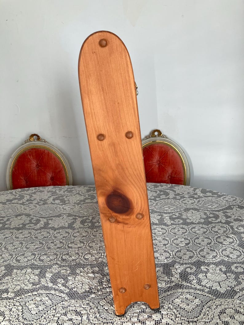 Puede incluir: Un soporte de madera con un acabado natural y una parte superior redondeada. El soporte tiene una serie de peque&ntilde;os clavos espaciados uniformemente a lo largo de los lados.