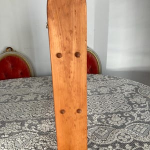 Puede incluir: Un tablero trasero de madera con la parte superior redondeada y la parte inferior plana. El tablero trasero es de color marr&oacute;n claro y tiene cinco agujeros espaciados uniformemente a lo largo del tablero.