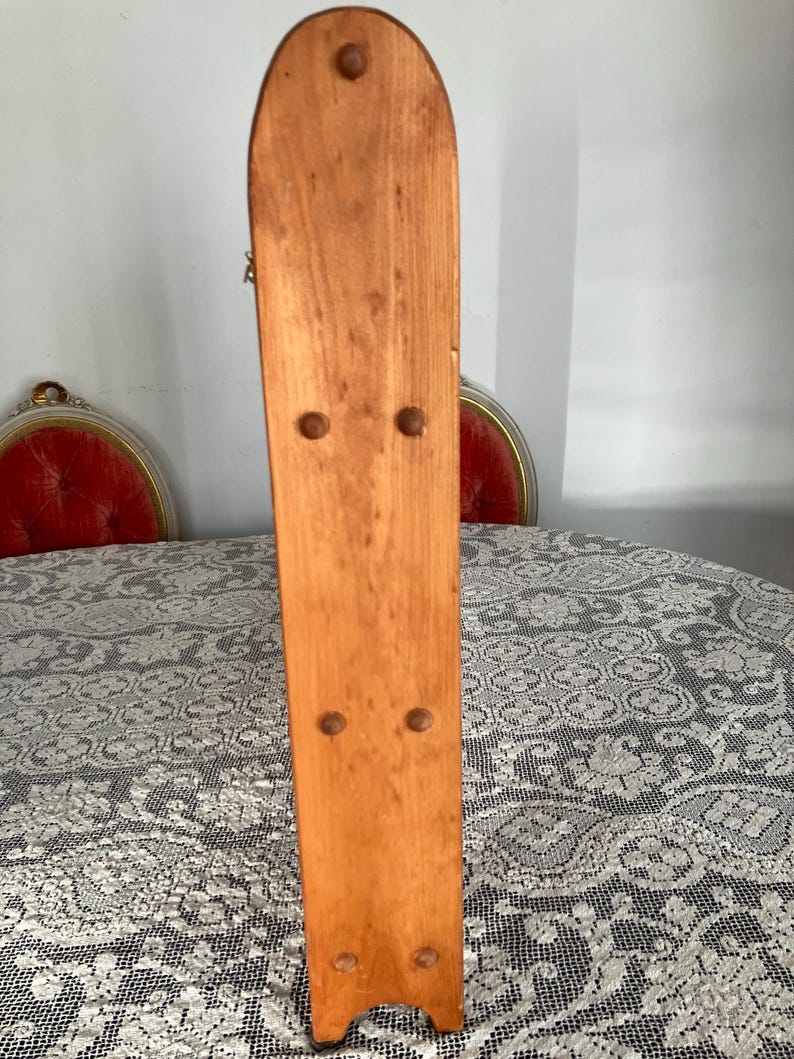 Puede incluir: Un tablero trasero de madera con la parte superior redondeada y la parte inferior plana. El tablero trasero es de color marr&oacute;n claro y tiene cinco agujeros espaciados uniformemente a lo largo del tablero.