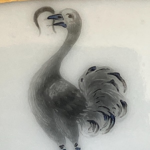 Puede incluir: Ilustración detallada de un pájaro gris con un cuello largo y una cola grande y adornada. El pájaro está sobre un fondo blanco, con un borde azul oscuro y adornos dorados.