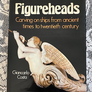 May include: A book titled "Figureheads" with the subtitle "Carving on ships from ancient times to twentieth century." The cover features a carved figurehead of a winged woman playing a horn against a black background. The author's name, Giancarlo Costa, is also displayed.