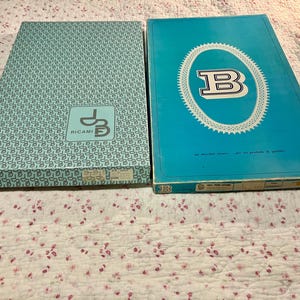 May include: Two vintage rectangular boxes. One is light blue with a repeating pattern and the text "RICAMI" and a logo. The other is turquoise with a white oval design and the letter "B".
