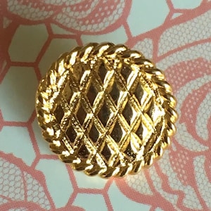May include: A gold-toned button with a rope-like border and a diamond-shaped pattern in the centre.