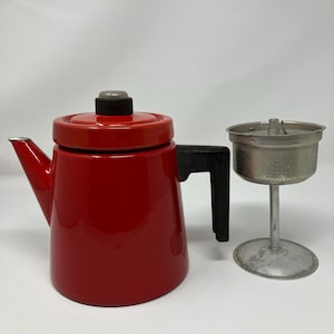 以下が含まれることがあります： 黒いハンドルと蓋が付いた、ヴィンテージの赤いエナメルコーヒーポット。別の金属製フィルターバスケットがポットの横にあります。コーヒーポットには注ぎ口が付いています。