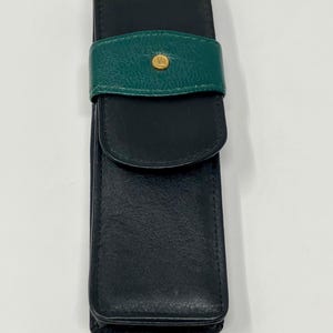 Op de afbeelding: Een zwart leren pennenetui met een groene leren klep en een gouden knoop.