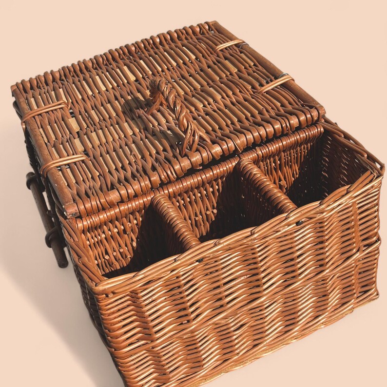 May include: A brown wicker picnic basket with a hinged lid and a woven handle. The basket has interior compartments, and the lid features a twisted handle. The basket is made of woven brown wicker.