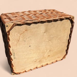 May include: A rectangular wicker basket with a light brown wooden base and sides. The basket's woven top and edges are a darker brown, creating a contrast. The basket appears to be empty.