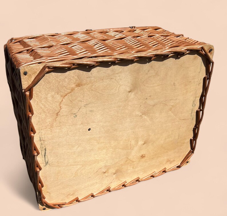 May include: A rectangular wicker basket with a light brown wooden base and sides. The basket's woven top and edges are a darker brown, creating a contrast. The basket appears to be empty.