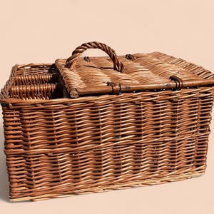May include: A rectangular brown wicker picnic basket with a hinged lid and a woven handle. The basket has a compartment for bottles and a secure latch. The basket is made of woven brown wicker.