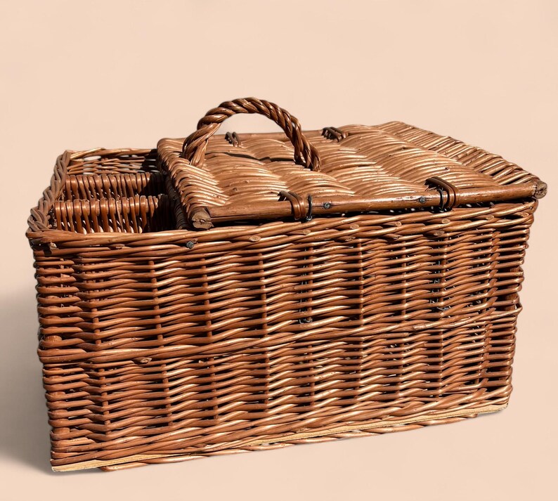 May include: A rectangular brown wicker picnic basket with a hinged lid and a woven handle. The basket has a compartment for bottles and a secure latch. The basket is made of woven brown wicker.