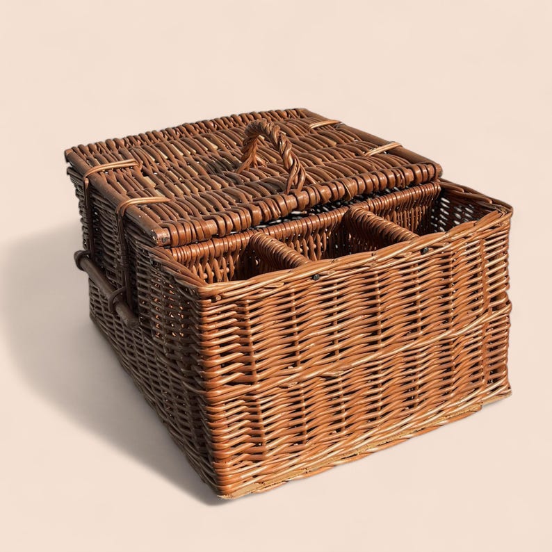 May include: A brown wicker picnic basket with a hinged lid and a woven handle. The interior is divided into compartments. The basket is made of woven brown wicker and has a rectangular shape.