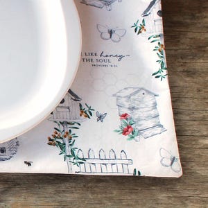 May include: White placemat with a beehive, flowers, butterflies, and a fence design. The placemat has the text "Like honey - to the soul" and "Proverbs 16:24" printed on it.