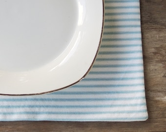 May include: A white ceramic plate with a gold rim sits on a blue and white striped placemat.