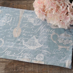 May include: A blue and white tea-themed table runner with a vintage design. The runner features a teapot, spoon, and handwritten text that says "Tea Time" and "Menu".