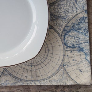May include: A white ceramic plate with a gold rim sits on a placemat with a blue and beige world map design.