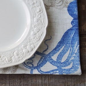 May include: A white, ornate plate with a floral design rests on a placemat featuring a blue octopus illustration. The placemat has a neutral background with a subtle pattern. The scene is set on a rustic, wooden surface.