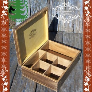 May include: A wooden box with a hinged lid and six compartments. The box is stained a dark brown colour and has a light brown interior. The lid has a decorative design on the inside.